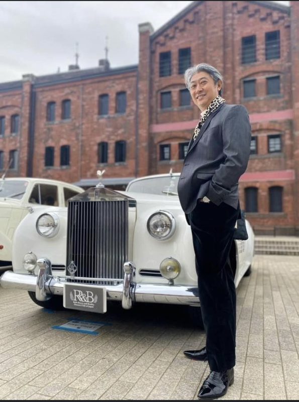 赤レンガ倉庫とクラシックカーの前に立つ西田理一郎