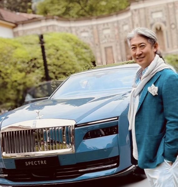 庭園で青い高級車の横に立つ西田理一郎