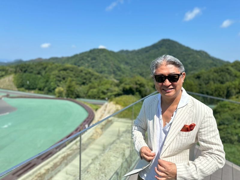 山と湖を望むテラスに立つ西田理一郎