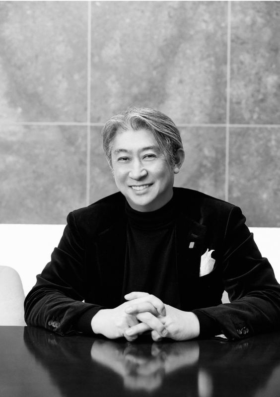 テーブルで手を組み微笑む西田理一郎のポートレート（モノクロ）
